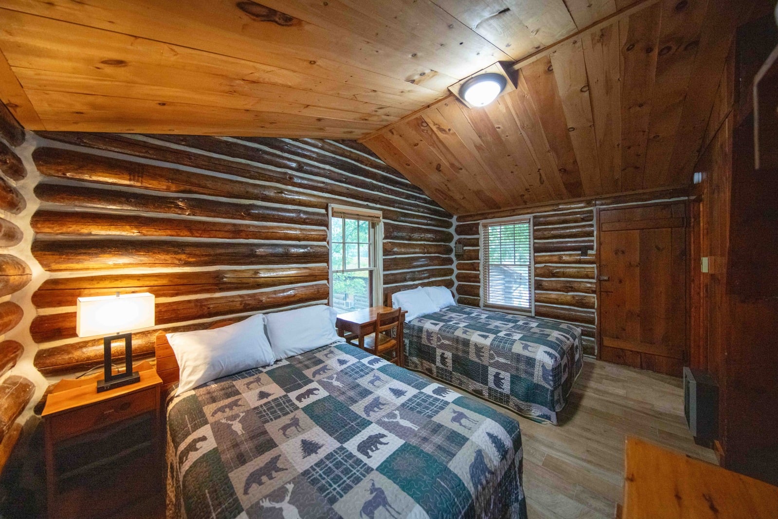 A log cabin room with two beds, a nightstand, and a lamp.