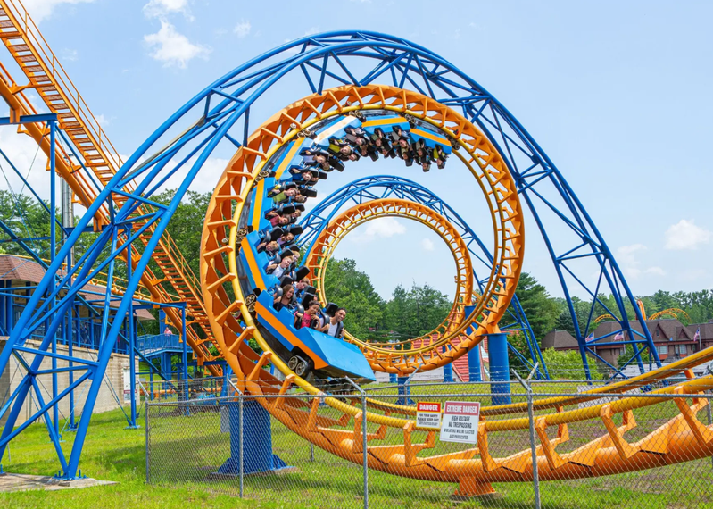 A blue and orange roller coaster with people riding it in a fenced area.