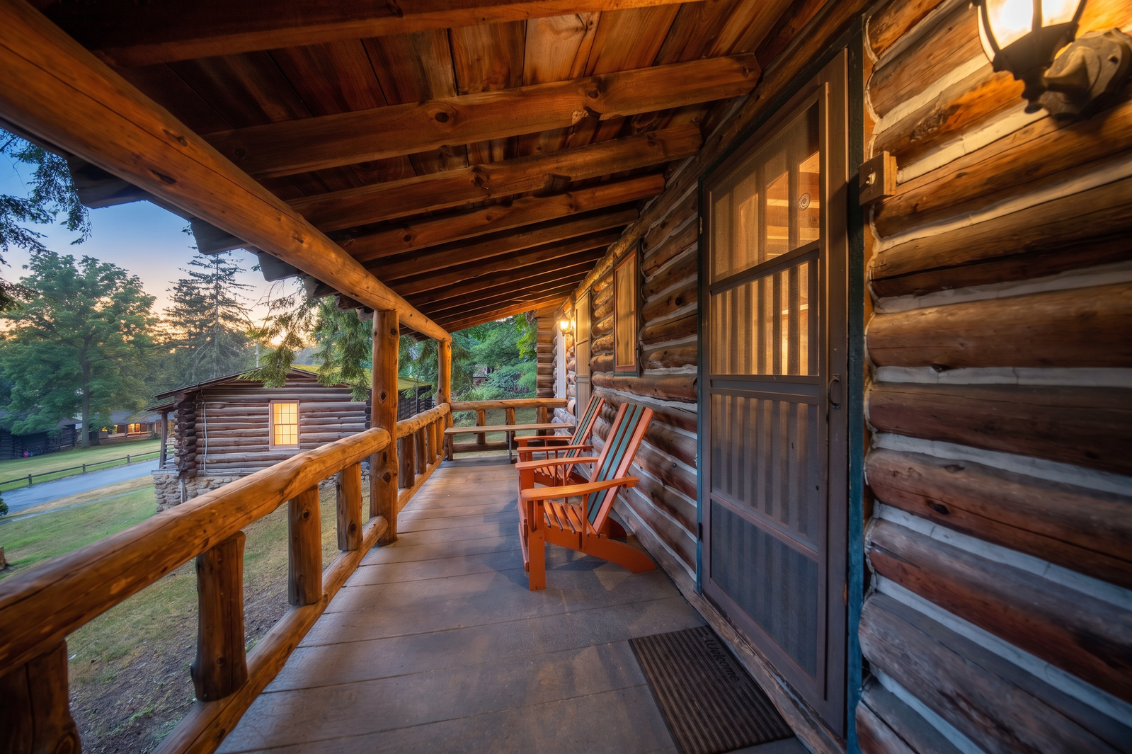 A log cabin porch with two wooden chairs and a view of the surrounding trees and grass.