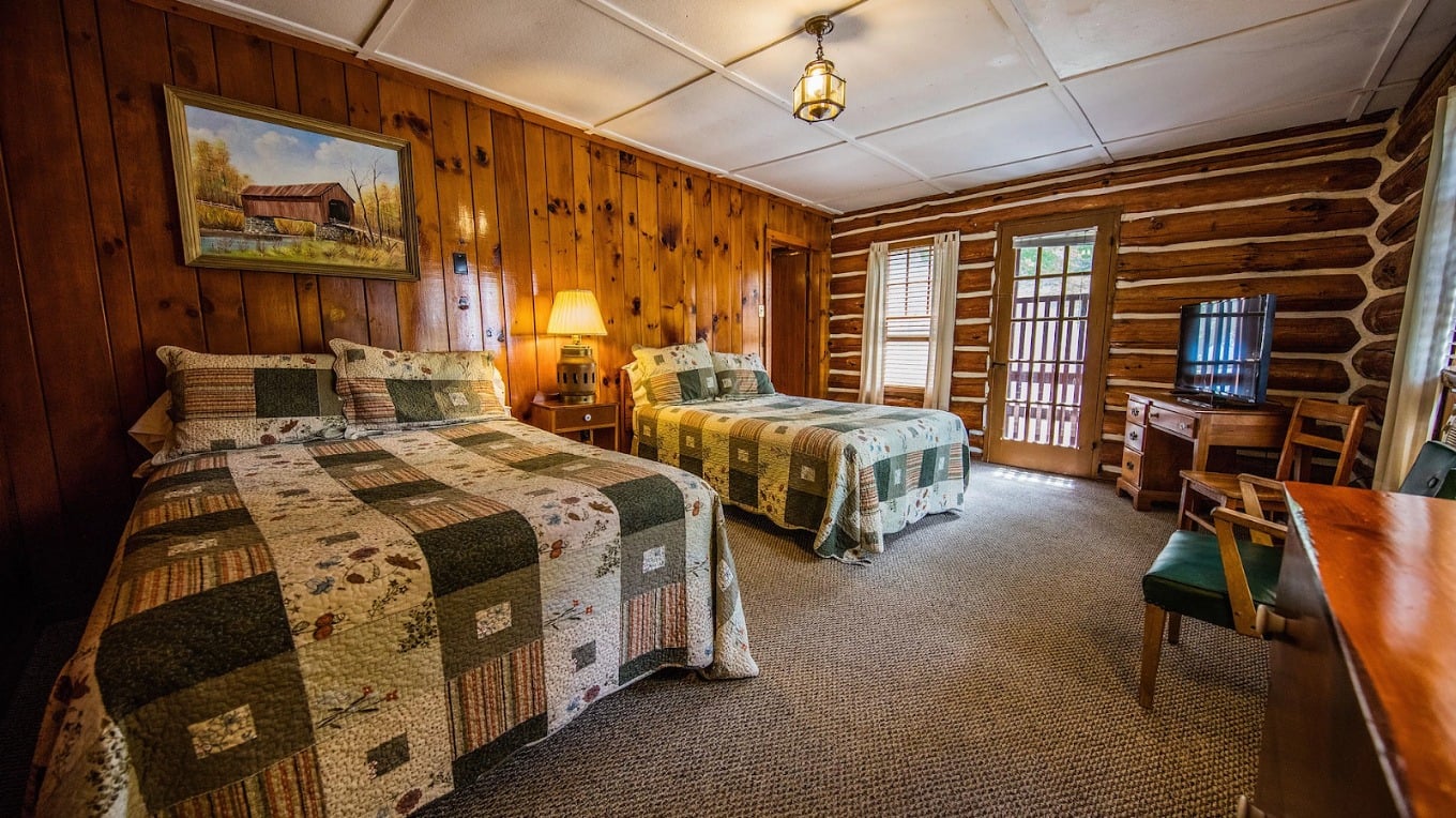 A cozy log cabin-style hotel room with two beds, a desk, and a TV.