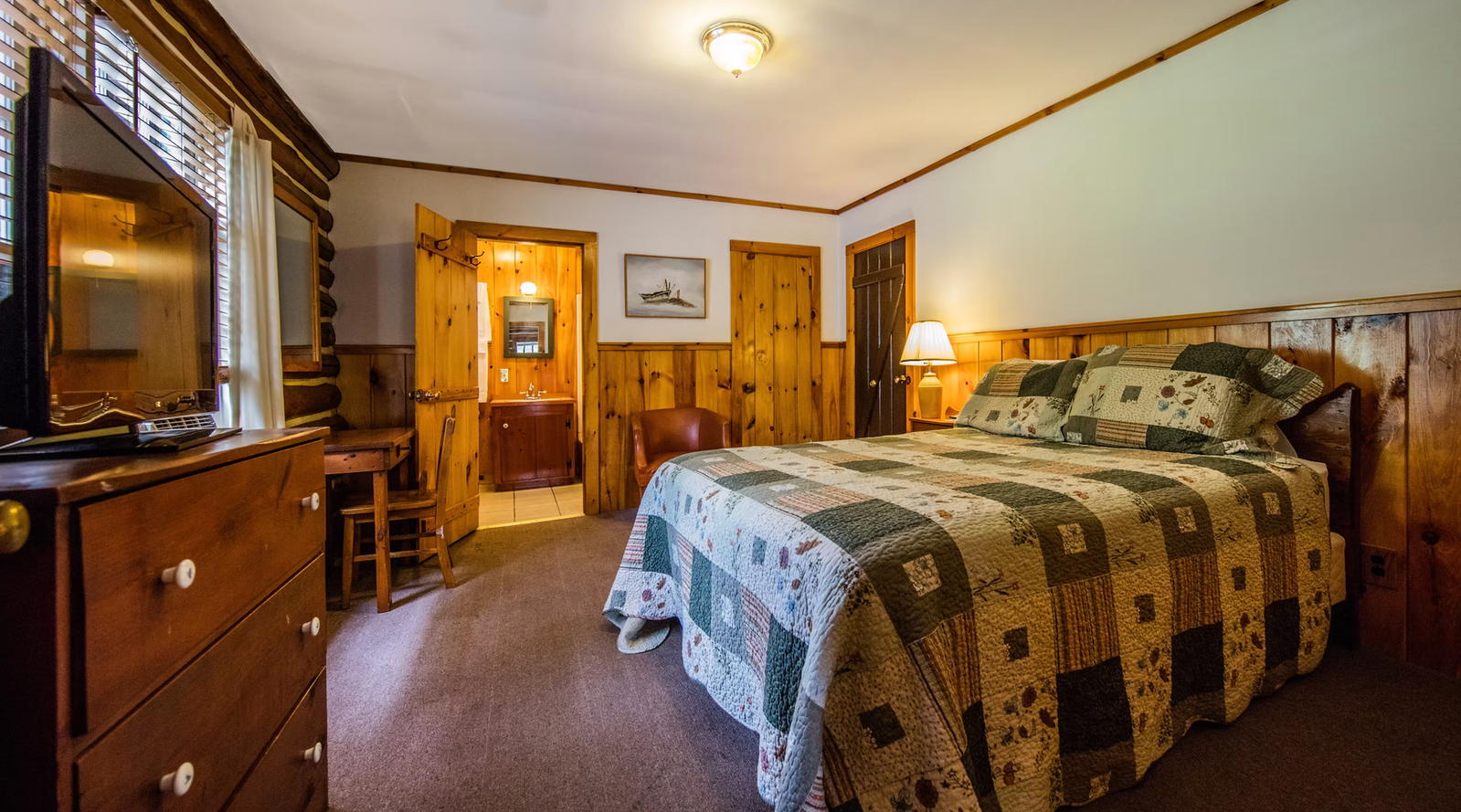 A wide-angle view of a hotel room with a bed, dresser, and desk.